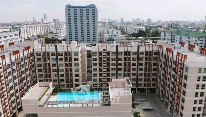 Stunning aerial view of modern apartment complex with rooftop pool and cityscape backdrop.