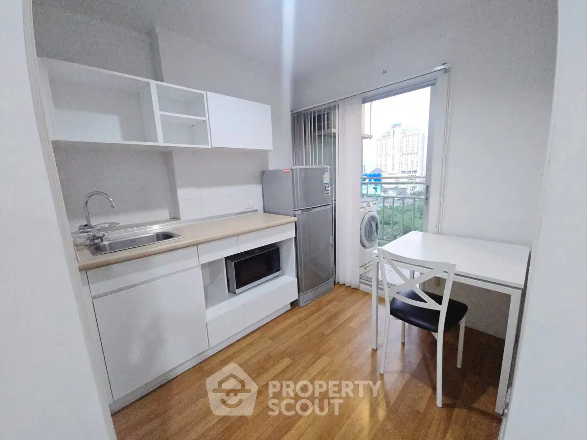 Modern kitchen with sleek white cabinets, compact dining area, and city view from window.