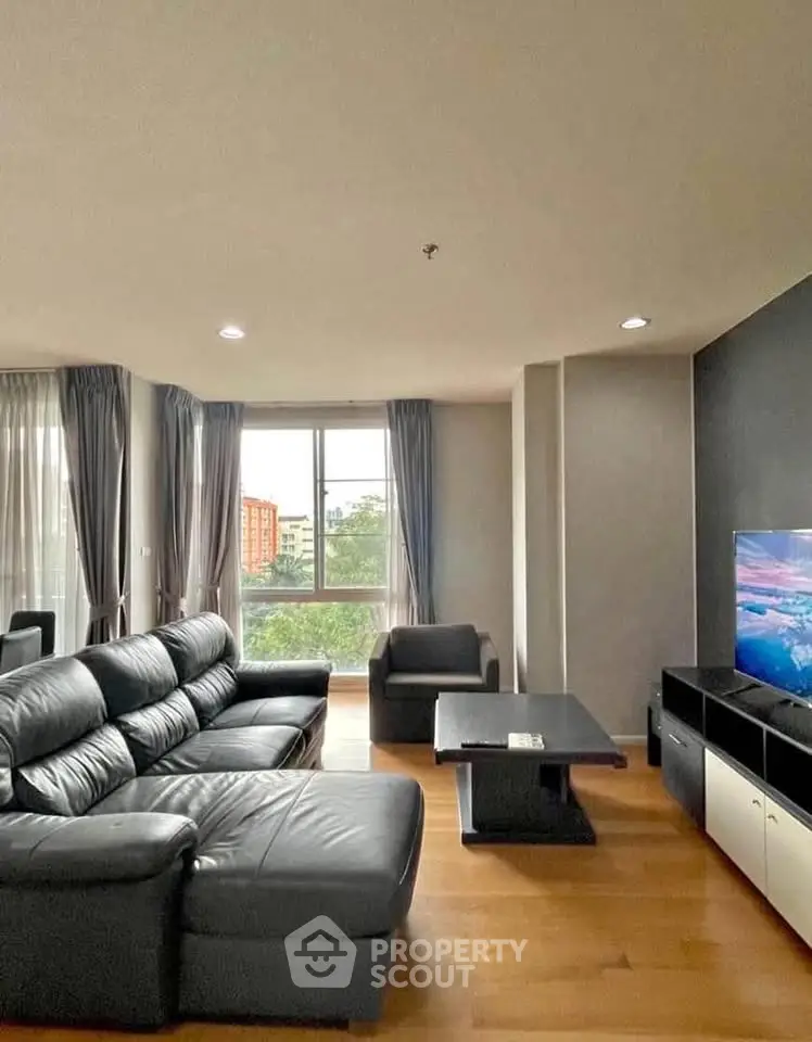 Spacious living room with modern black leather sofa and large window view.
