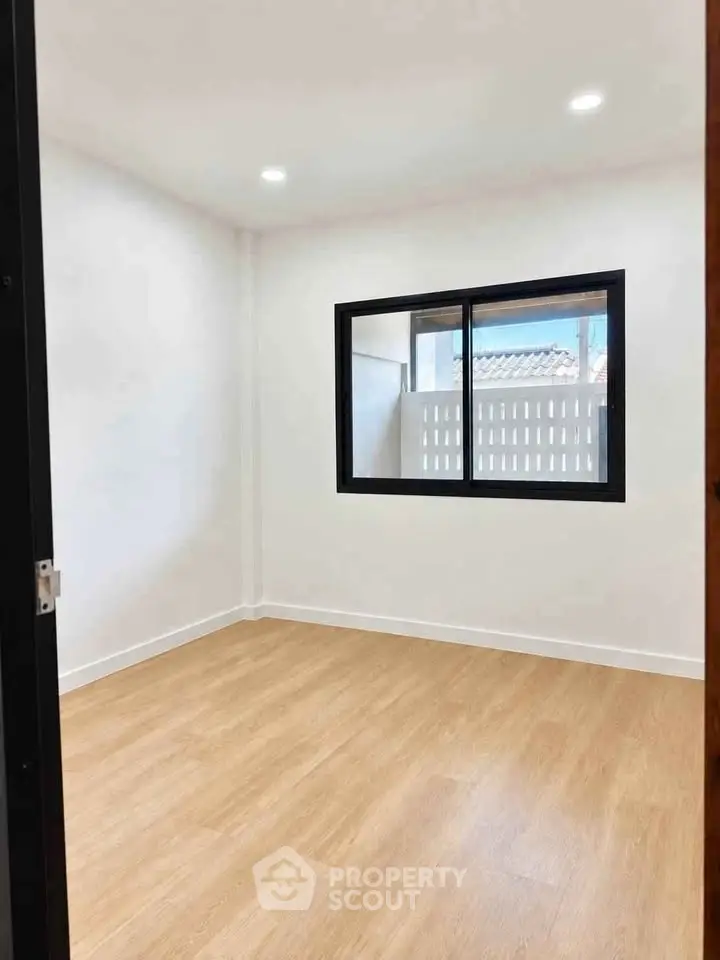Spacious unfurnished room with wooden flooring and large window, perfect for customization.