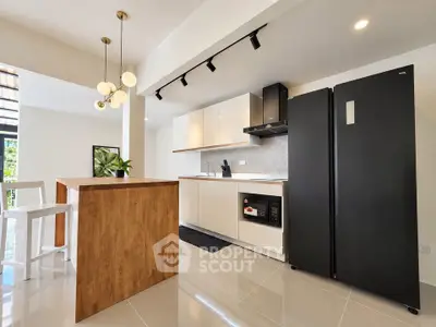 Modern kitchen with sleek black fridge and stylish lighting in contemporary home.