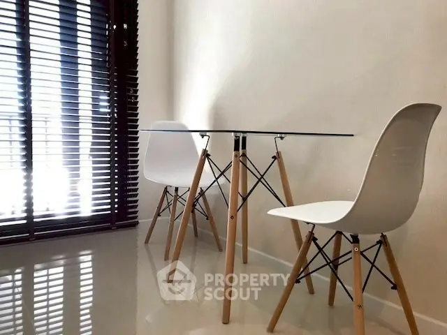 Modern minimalist dining area with glass table and stylish chairs near large window.