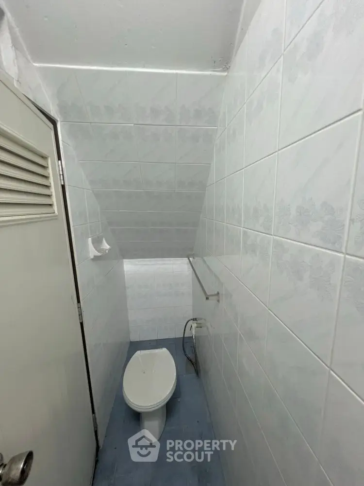 Compact bathroom with tiled walls and sloped ceiling, featuring a toilet and minimalistic design.
