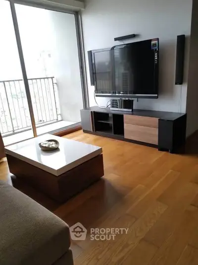 Modern living room with sleek TV setup and wooden flooring, featuring a balcony view.