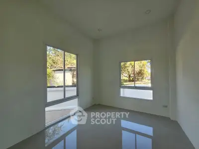 Spacious empty room with large windows and glossy tiled floor, offering abundant natural light and garden view.