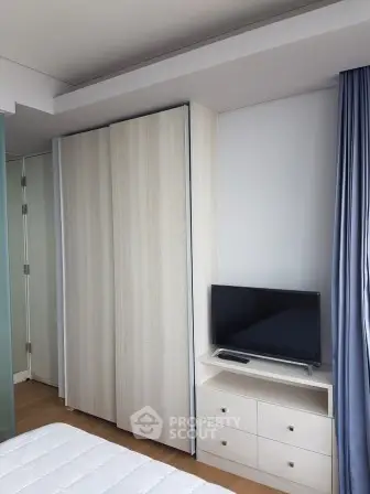 Modern bedroom with sleek wardrobe and compact TV unit, featuring minimalist design and natural light.