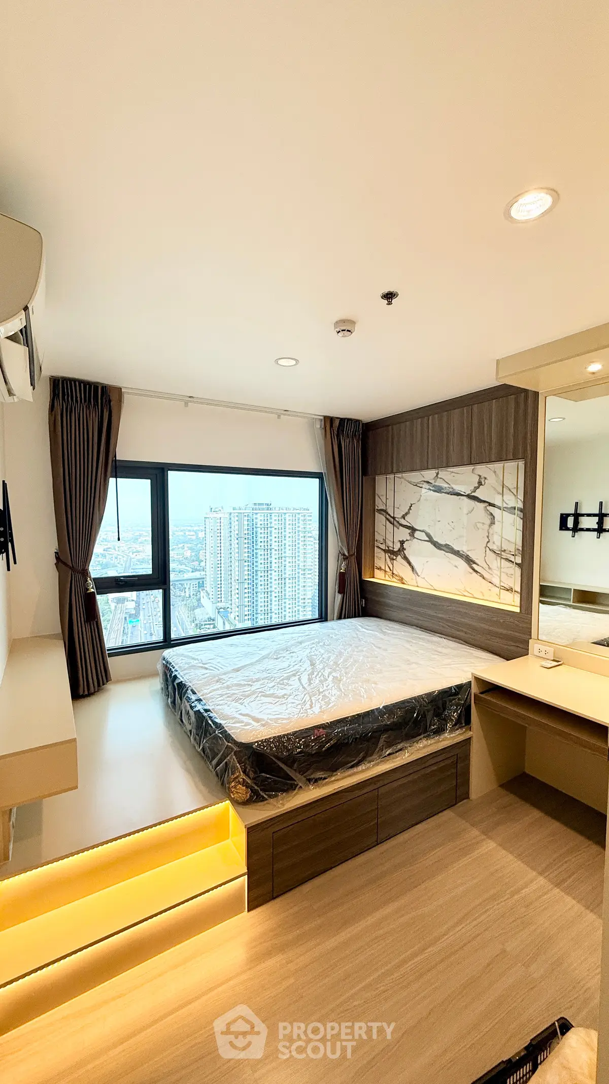 Modern bedroom with large window offering stunning city view, featuring sleek design and built-in storage.