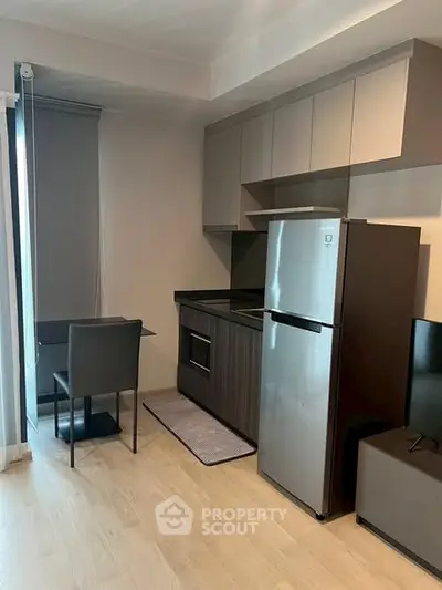 Modern kitchen with sleek cabinets, stainless steel fridge, and cozy dining area in a stylish apartment.