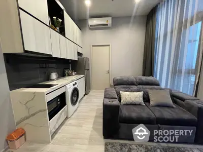 Modern living room with sleek kitchen, featuring washing machine and stylish sofa.