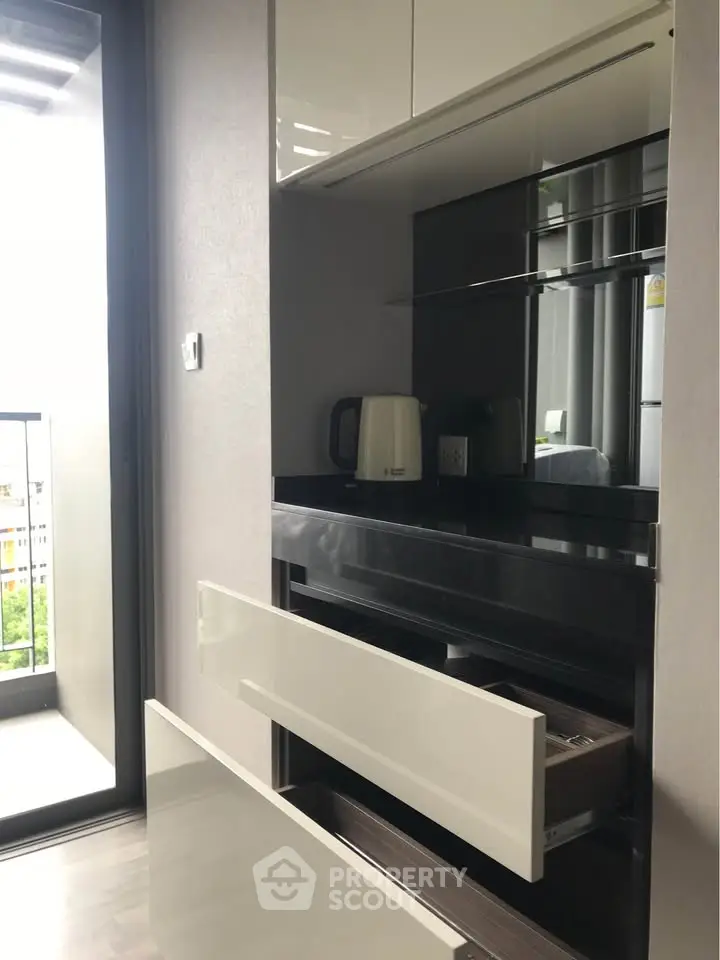 Modern kitchen with sleek cabinetry and balcony view, featuring a kettle and ample storage space.