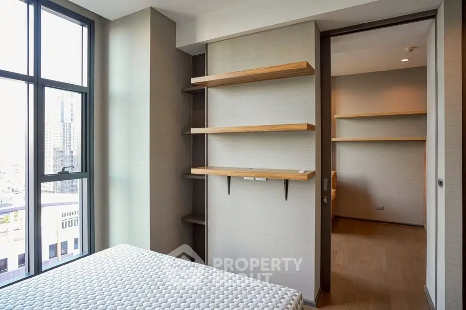 Modern bedroom with large windows and built-in shelves, offering ample natural light and storage space.