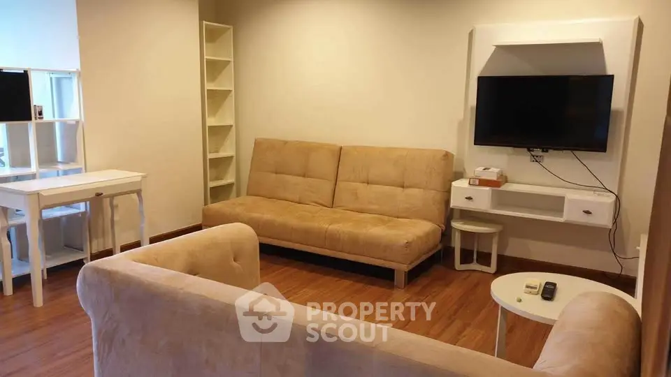 Cozy living room with beige sofas, wall-mounted TV, and wooden flooring for a warm ambiance.