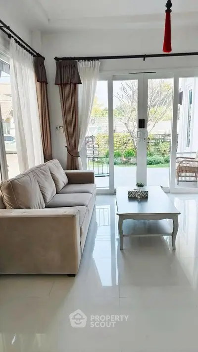 Bright living room with large windows and garden view, featuring a cozy sofa and elegant coffee table.