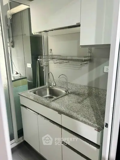 Compact modern kitchen with granite countertop and stainless steel sink in a cozy apartment.