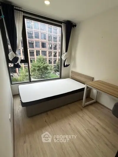 Modern bedroom with large window and city view, featuring a single bed and wooden desk.