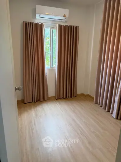 Cozy empty room with wooden flooring and air conditioning, perfect for a small bedroom or study.