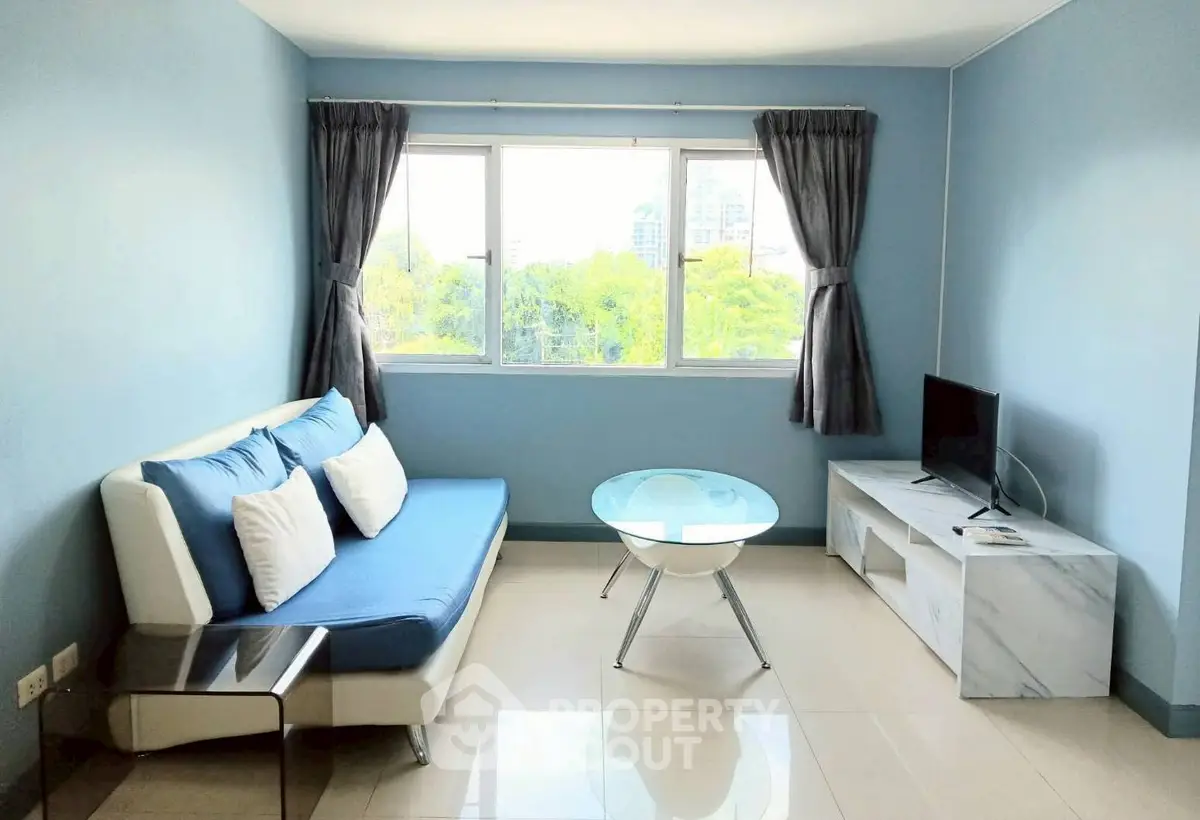 Bright living room with modern sofa, glass coffee table, and TV stand, featuring large window with city view.