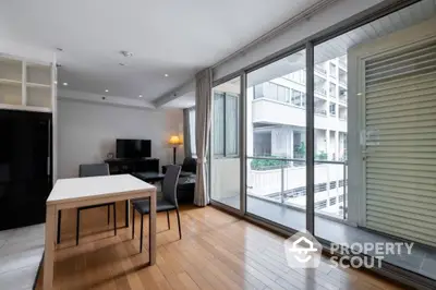 Spacious modern living room with large windows leading to a sunny balcony, sleek hardwood floors, and contemporary furnishings.