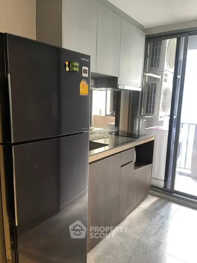 Modern kitchen with sleek black fridge and glass sliding doors leading to balcony.