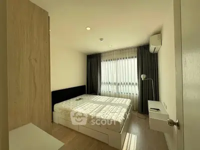 Modern bedroom with natural light, featuring a cozy bed, sleek furniture, and air conditioning.