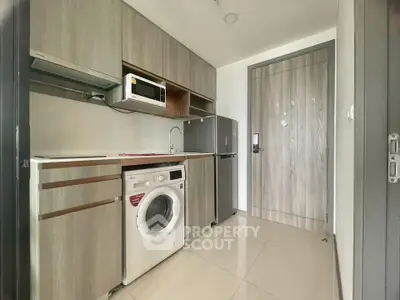 Modern compact kitchen with washing machine and microwave in sleek apartment.