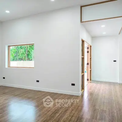 Spacious modern living room with wooden flooring and large window offering natural light.