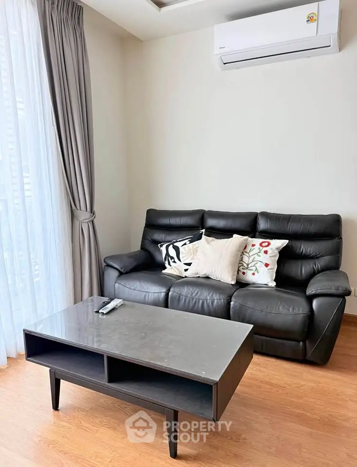 Modern living room with black leather sofa, sleek coffee table, and air conditioning unit.