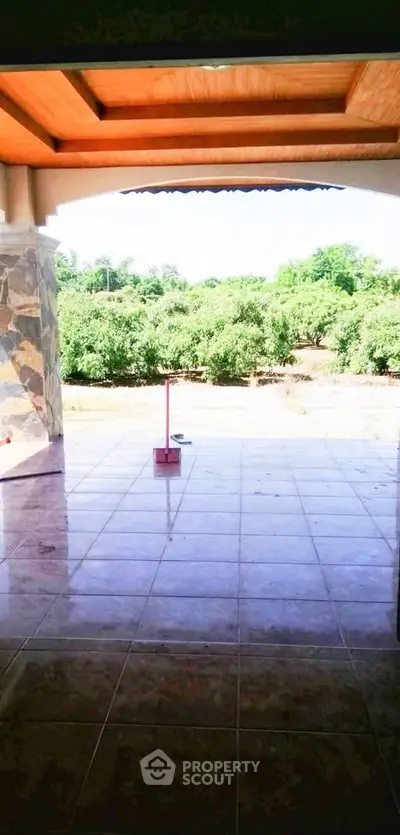 Spacious tiled patio with scenic garden view and wooden ceiling accents.