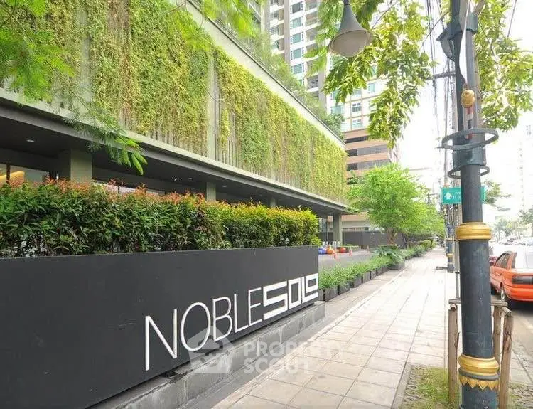Modern building exterior with lush greenery and stylish signage on a city sidewalk.