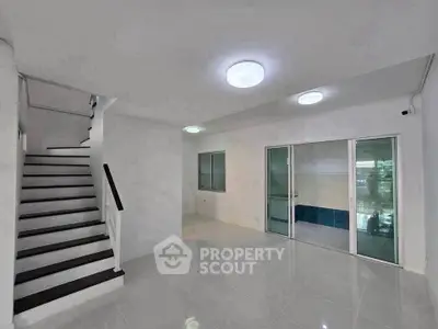 Spacious modern living room with sleek staircase and glass doors leading to a bright area.