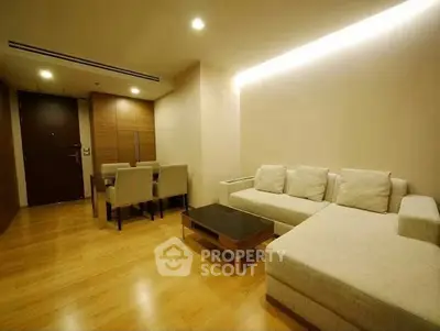 Modern living room with cozy sectional sofa and elegant dining area, featuring warm wooden flooring and ambient lighting.