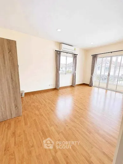 Spacious empty room with wooden flooring and large windows for natural light.