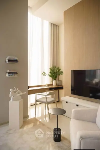 Elegant living room with modern decor, featuring a TV, stylish furniture, and natural light from large windows.