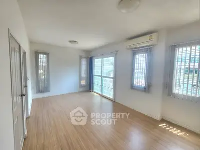 Spacious empty room with wooden flooring and large windows, perfect for customization.