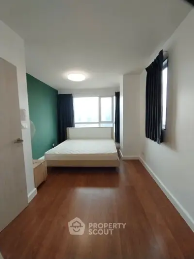 Spacious bedroom with wooden flooring and large windows for natural light