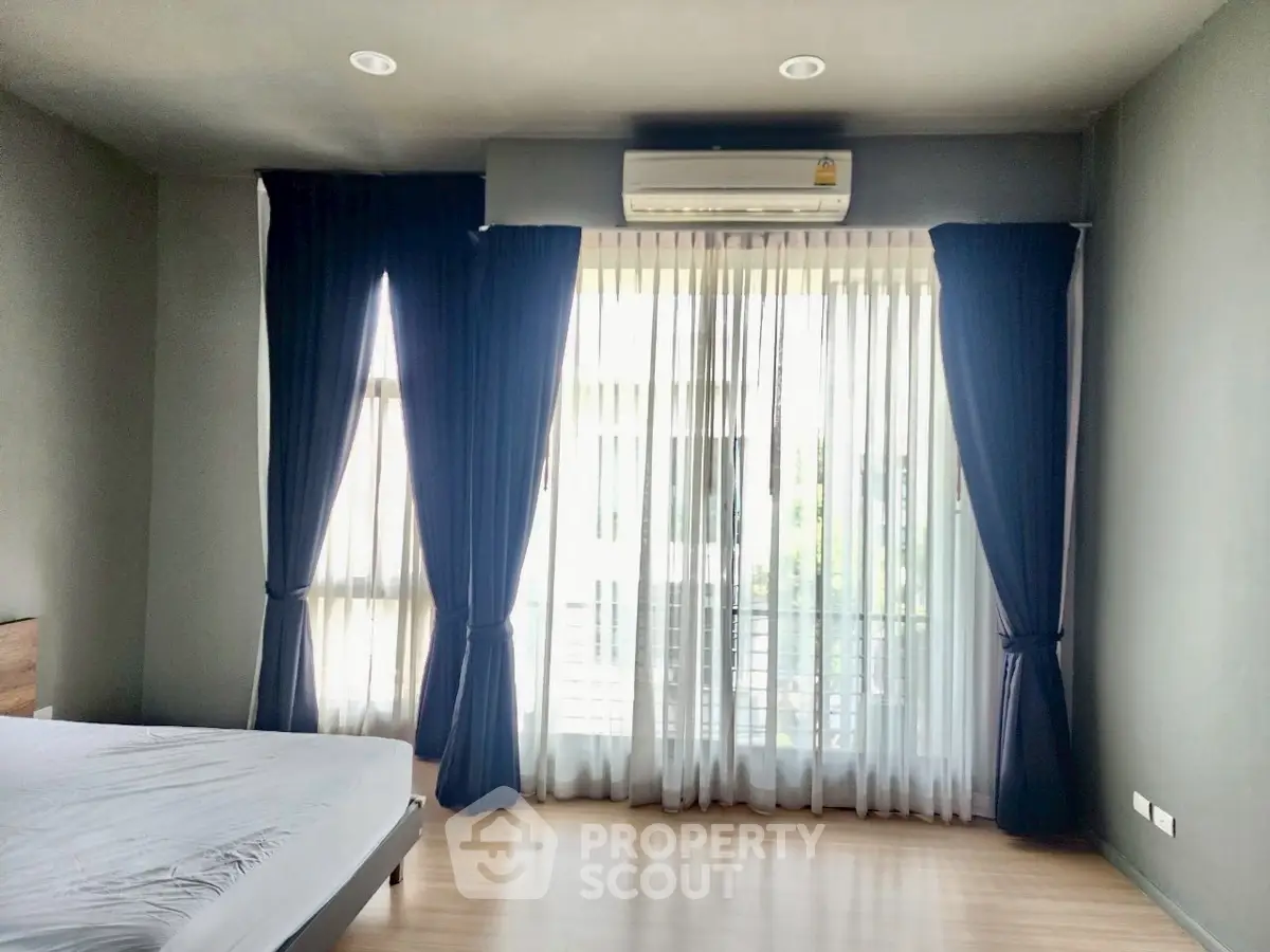 Spacious bedroom with large windows and elegant curtains, featuring a modern air conditioning unit.