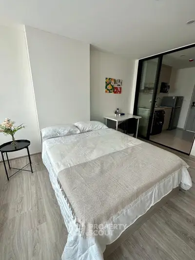Modern bedroom with cozy bed and sliding glass door to kitchen area, perfect for urban living.