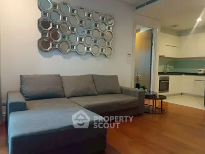 Modern living room with stylish mirror and cozy gray sofa, adjacent to a sleek kitchen area.