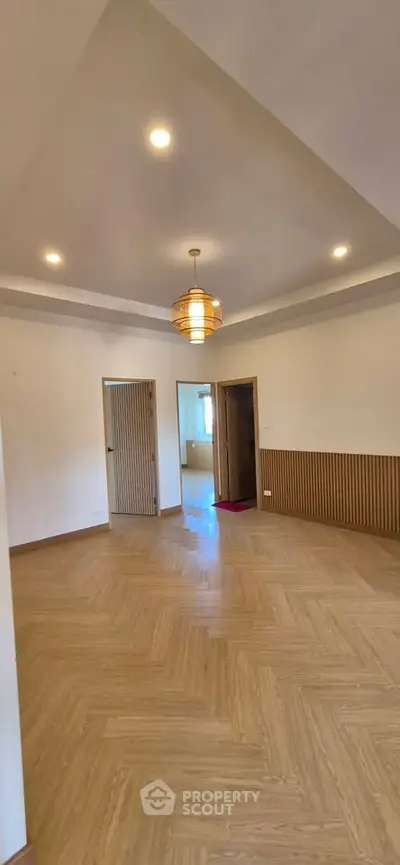 Spacious empty room with elegant wooden flooring and modern ceiling lights.