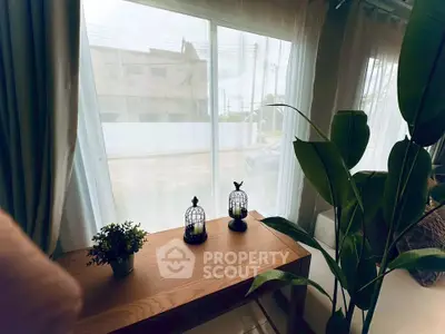 Charming living room with large window and elegant decor, featuring lush indoor plants and stylish wooden furniture.