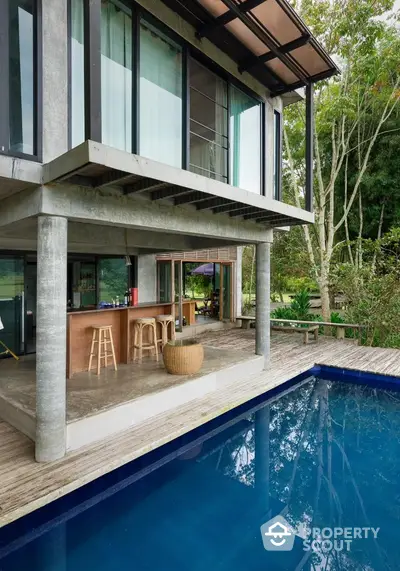 Modern luxury home with pool and open-air bar area, surrounded by lush greenery.