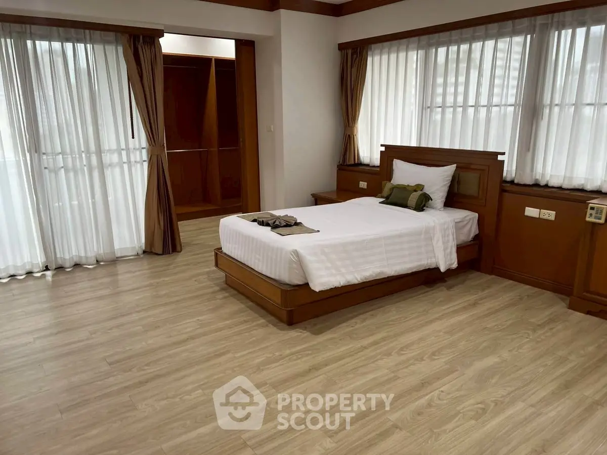 Spacious bedroom with elegant wooden flooring and large windows for natural light.