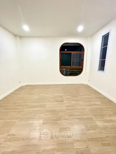 Spacious empty room with elegant wooden flooring and unique arched window design.