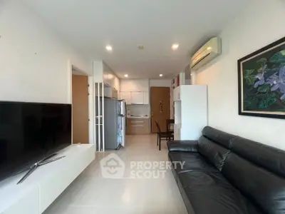 Modern living room with sleek black leather sofa, large TV, and compact kitchen area.