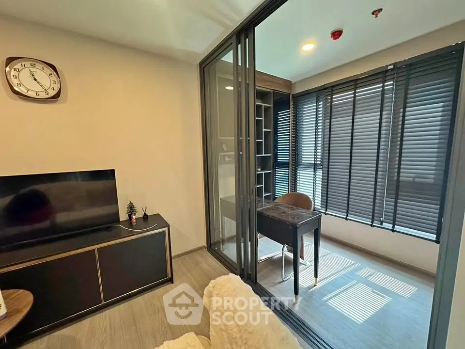 Modern living room with study area, featuring sleek furniture and large windows with blinds.
