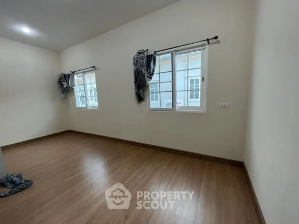 Spacious empty room with wooden flooring and large windows for natural light.