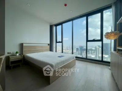 Spacious bedroom with floor-to-ceiling windows offering stunning city views, modern furnishings, and natural light.