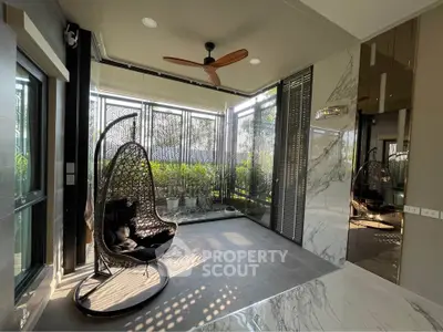 Luxurious modern interior with hanging chair and large windows overlooking greenery, perfect for relaxation.