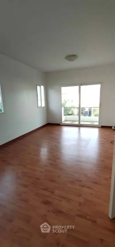 Spacious empty living room with wooden flooring and large windows for natural light.