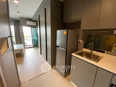 Modern apartment kitchen with sleek cabinetry and stainless steel appliances, leading to a bright living area.